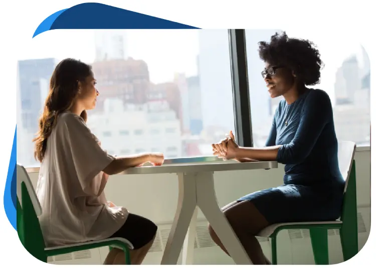 Two women sitting at a table talking to each other.